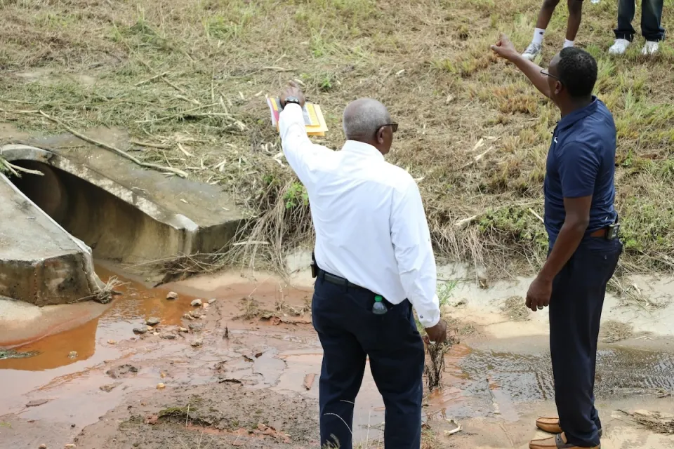 Two men in collared shirts and slacks looking and pointing at drainage ditch.